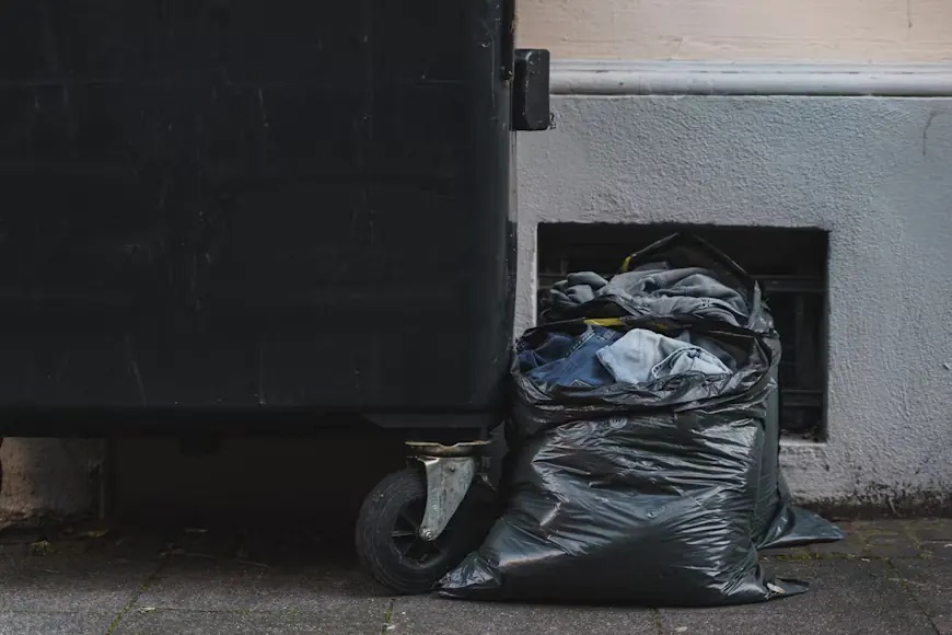 Black trash bags of cleanout waste beside a wheeled dumpster