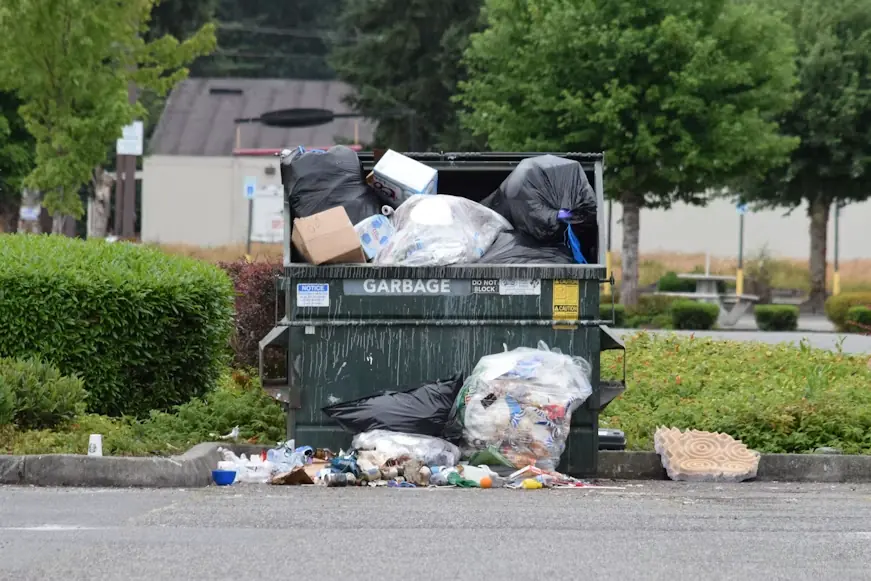Overflowing garbage dumpster with bags and trash on the ground around it